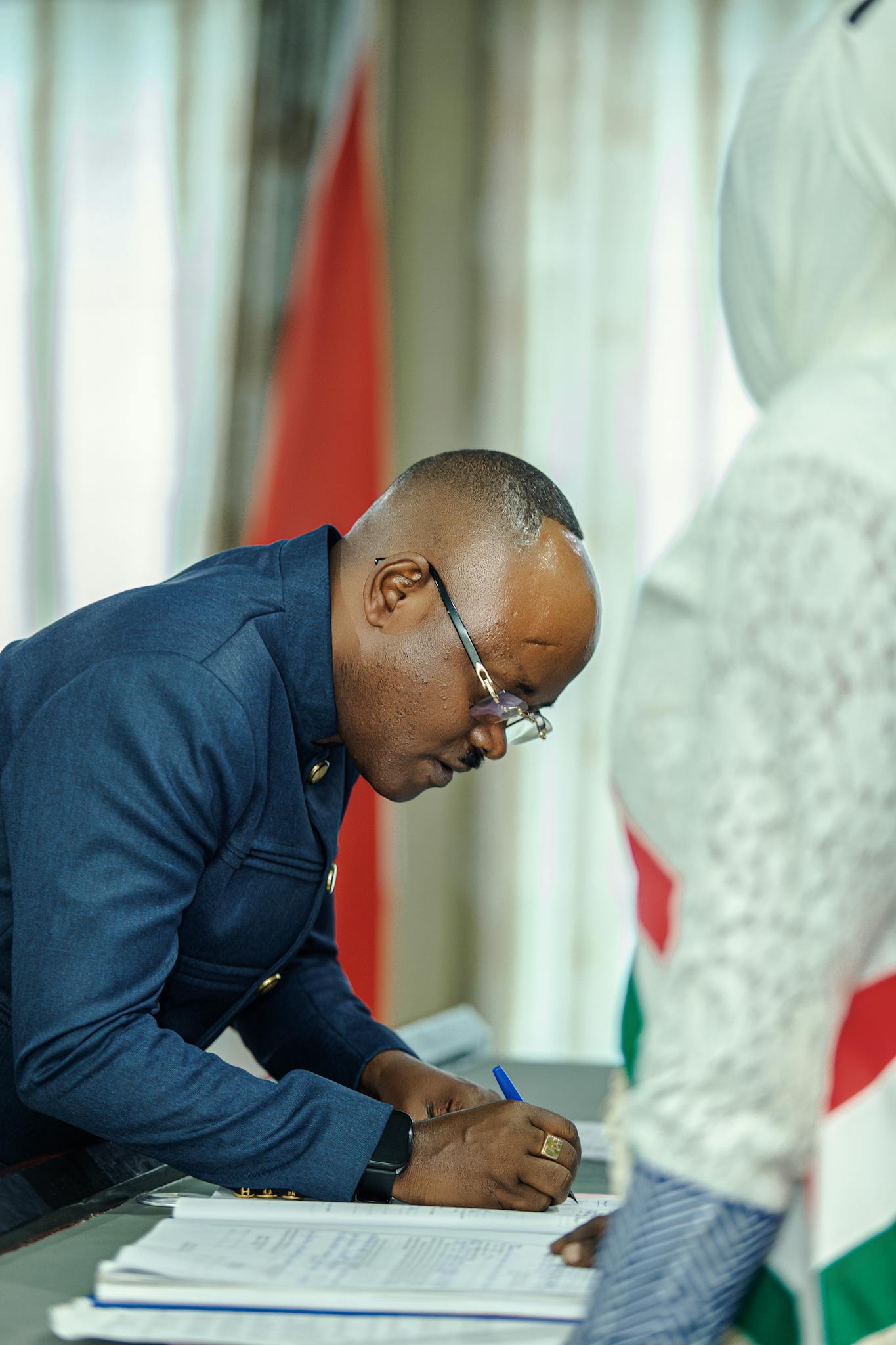 A man in formal attire signing documents during an official ceremony in an office setting.