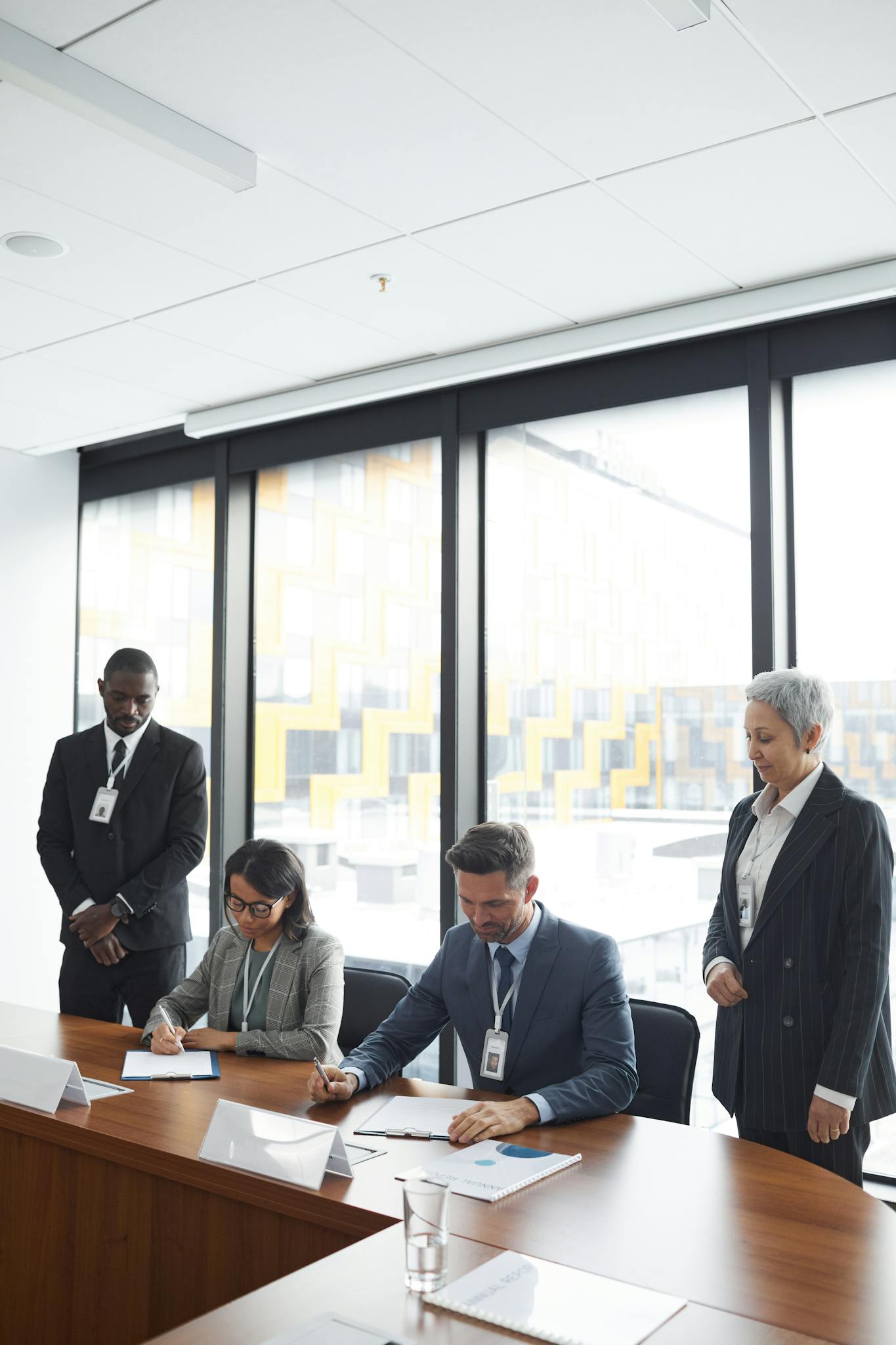 A diverse business team signing contracts in a modern conference room with a cityscape view.